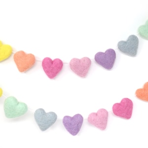 May include: Two strands of felt heart garlands in pastel colors, including yellow, orange, pink, purple, and blue-green. The hearts are strung on white thread, creating a festive and decorative item.