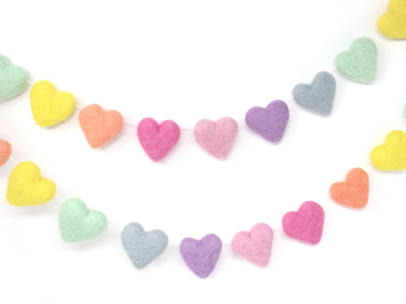 May include: Two strands of felt heart garlands in pastel colors, including yellow, orange, pink, purple, and blue-green. The hearts are strung on white thread, creating a festive and decorative item.