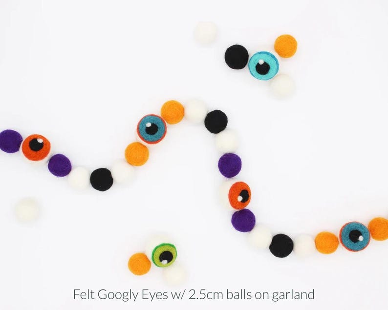 Peut inclure: Une guirlande compos&eacute;e de boules en feutrine de 2,5 cm de couleur orange, noire, blanche et violette, altern&eacute;es avec des yeux mobiles en feutrine bleus, verts et orange. Le texte "Felt Googly Eyes w/ 2.5cm balls on garland" est inscrit en bas.