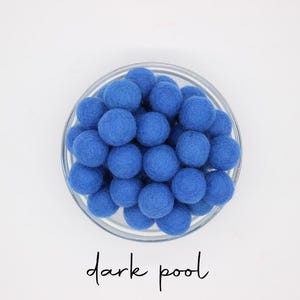 May include: A glass bowl filled with dark blue felt balls. The balls are closely packed, forming a textured, spherical arrangement. The words "dark pool" are written in cursive script below the bowl.