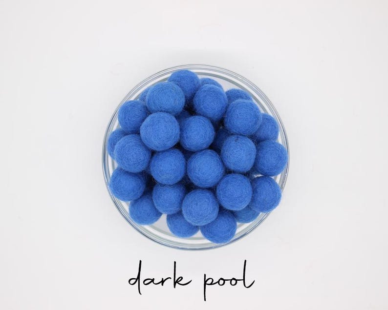 May include: A glass bowl filled with dark blue felt balls. The balls are closely packed, forming a textured, spherical arrangement. The words "dark pool" are written in cursive script below the bowl.
