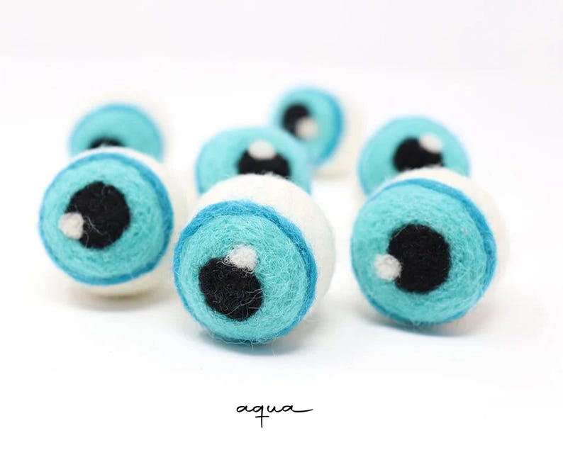 Peut inclure: Un ensemble de boules en laine feutr&eacute;e sph&eacute;riques ressemblant &agrave; des globes oculaires. Chaque boule pr&eacute;sente une base blanche, un iris bleu aqua vif, une pupille noire et un petit point blanc brillant. Le texte aqua est inscrit en bas.