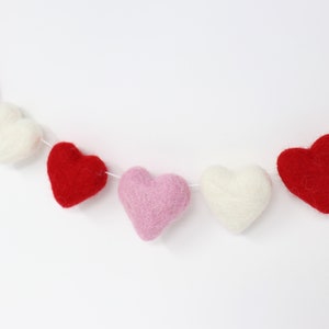 May include: A garland of felt hearts in pink, red, and white. The hearts are strung together with white thread and are arranged in a repeating pattern.