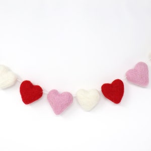 May include: A garland of felt hearts in red, pink, and white. The hearts are strung together with white thread and are arranged in a repeating pattern.