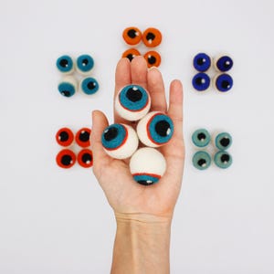 Peut inclure: Une collection de globes oculaires en laine feutr&eacute;e, ronds et de diff&eacute;rentes couleurs, notamment bleu, orange, rouge et sarcelle. Chaque globe oculaire pr&eacute;sente une scl&eacute;rotique blanche, un iris color&eacute;, une pupille noire et un petit reflet blanc.