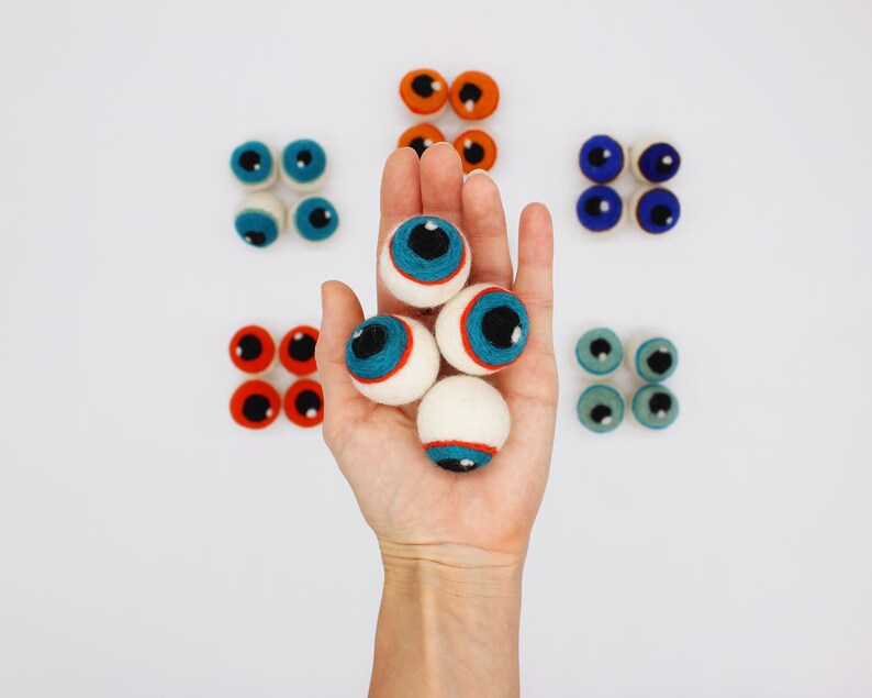 Peut inclure: Une collection de globes oculaires en laine feutr&eacute;e, ronds et de diff&eacute;rentes couleurs, notamment bleu, orange, rouge et sarcelle. Chaque globe oculaire pr&eacute;sente une scl&eacute;rotique blanche, un iris color&eacute;, une pupille noire et un petit reflet blanc.
