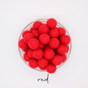 May include: A glass bowl containing many bright red felt balls. The word "red" is written in cursive script beneath the bowl. The balls are uniform in size and closely arranged.