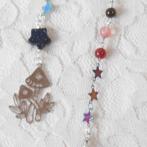 May include: A silver chain with iridescent stars and colorful beads, ending with a silver-capped, iridescent, pointed crystal pendulum. The chain also features a silver mushroom charm.
