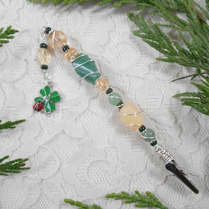 May include: A silver wire-wrapped bookmark with a green four-leaf clover charm and a variety of green, orange, and yellow gemstone beads.