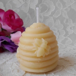 K&ouml;nnte beinhalten: Eine kleine, gelbe Bienenwachskerze in Form einer Honigwabe mit einem wei&szlig;en Docht. Die Kerze hat ein Bienenmotiv auf der Vorderseite.