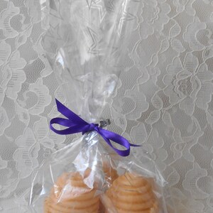K&ouml;nnte beinhalten: Zwei runde, geschichtete, honigfarbene Kerzen, verpackt in durchsichtigem Cellophan mit einem violetten Band.
