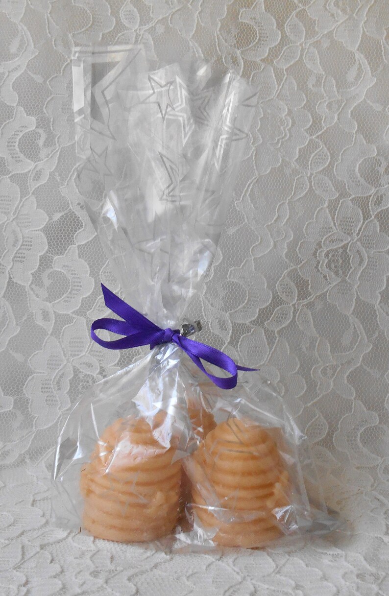 K&ouml;nnte beinhalten: Zwei runde, geschichtete, honigfarbene Kerzen, verpackt in durchsichtigem Cellophan mit einem violetten Band.