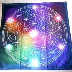 May include: A tapestry featuring a colorful, rainbow-hued background with a white geometric flower of life design. The design is surrounded by a circle of white dots.