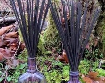 May include: Two glass bottles with purple and clear glass, filled with bundles of black incense sticks.