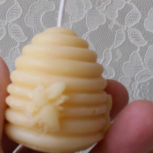 K&ouml;nnte beinhalten: Eine kleine, gelbe Bienenwachskerze in Form einer Wabe mit einem Bienendesign. Die Kerze hat einen wei&szlig;en Docht.