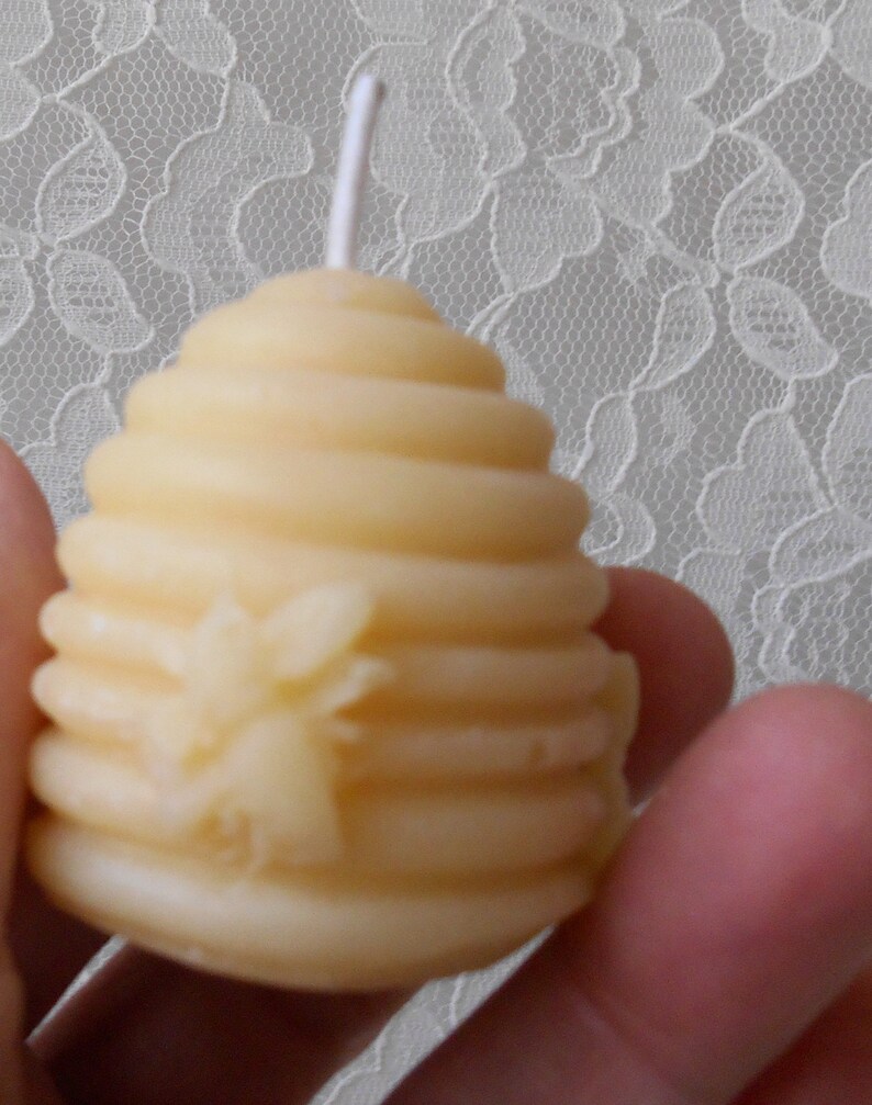 K&ouml;nnte beinhalten: Eine kleine, gelbe Bienenwachskerze in Form einer Wabe mit einem Bienendesign. Die Kerze hat einen wei&szlig;en Docht.