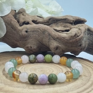Puede incluir: Un brazalete hecho de cuentas de piedras preciosas de varios colores, incluyendo verde, blanco, marr&oacute;n y morado. El brazalete est&aacute; sobre una superficie de madera.