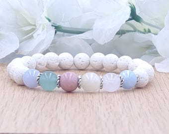 May include: A beaded bracelet featuring white lava rock beads and a series of pastel-colored gemstone beads. The bracelet includes light blue, green, pink, cream, and light pink beads, separated by silver-colored spacers. The bracelet is displayed on a wooden surface.