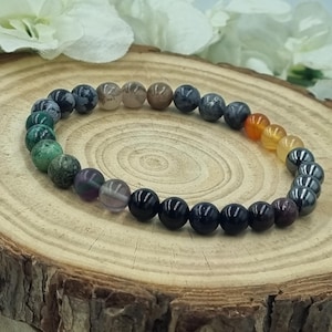 Könnte beinhalten: Ein mehrfarbiges Perlenarmband mit schwarzen, grauen, grünen, violetten, orangefarbenen und braunen Perlen. Das Armband liegt auf einer Holzoberfläche.