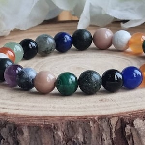May include: A colorful beaded bracelet with various stones, including green, blue, black, white, and brown. The bracelet is on a wooden surface.