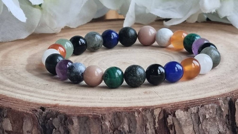 May include: A colorful beaded bracelet with various stones, including green, blue, black, white, and brown. The bracelet is on a wooden surface.