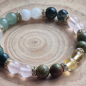 May include: A multi-colored gemstone bracelet with white, green, pink, and yellow beads. The beads are separated by gold spacers with clear rhinestones.