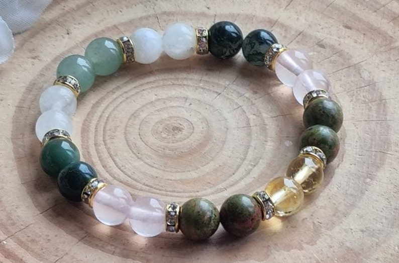 May include: A multi-colored gemstone bracelet with white, green, pink, and yellow beads. The beads are separated by gold spacers with clear rhinestones.