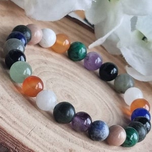 May include: A bracelet made of various colored gemstone beads, including green, blue, orange, and purple. The bracelet is on a wooden surface.
