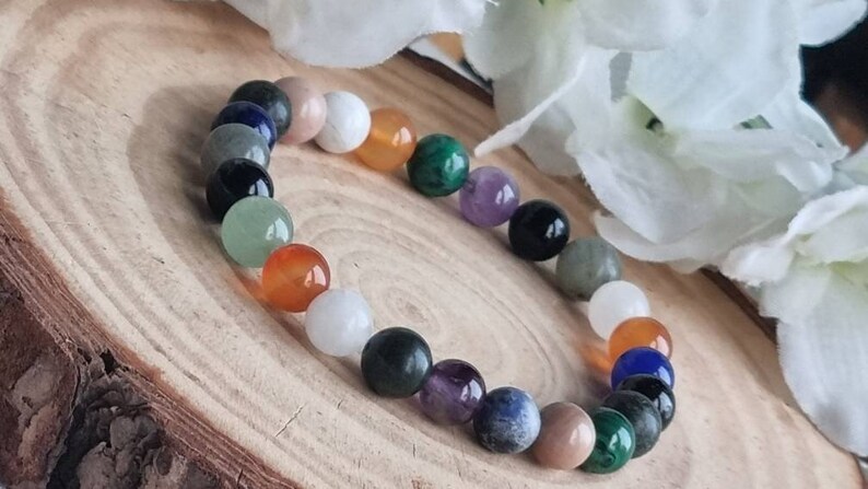 May include: A bracelet made of various colored gemstone beads, including green, blue, orange, and purple. The bracelet is on a wooden surface.