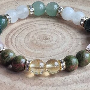 May include: A bracelet made of various gemstones, including green aventurine, white moonstone, rose quartz, and citrine. The bracelet is accented with gold-toned beads and clear crystals.
