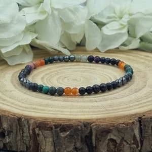 Könnte beinhalten: Ein mehrfarbiges Perlenarmband mit schwarzen, grauen, grünen und orangefarbenen Perlen. Das Armband liegt auf einer Holzoberfläche.