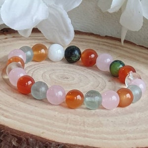 May include: A bracelet made of various colored beads, including pink, orange, green, and white. The beads are round and smooth, and the bracelet is strung on a clear elastic cord.