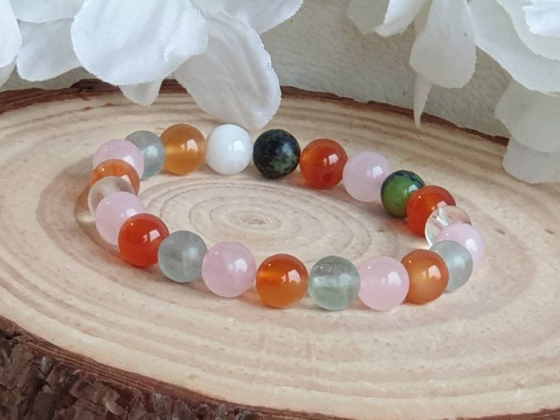 May include: A bracelet made of various colored beads, including pink, orange, green, and white. The beads are round and smooth, and the bracelet is strung on a clear elastic cord.