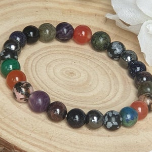 Op de afbeelding: Een armband gemaakt van verschillende halfedelstenen, waaronder amethist, carneol en groene aventurijn. De armband ligt op een houten oppervlak.