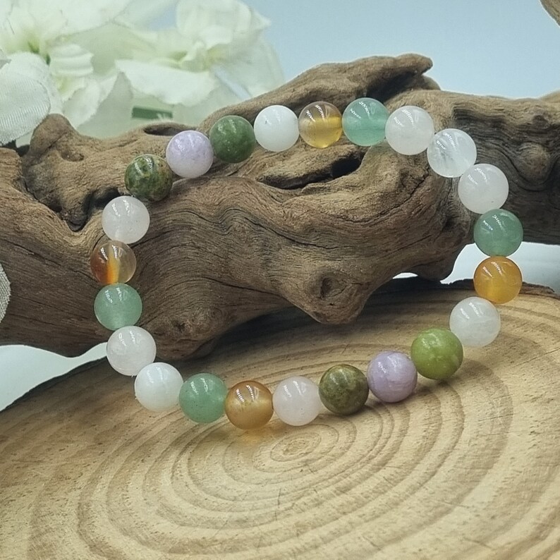 Puede incluir: Un brazalete hecho de cuentas de piedras preciosas de varios colores, incluyendo verde, blanco, rosa y naranja. Las cuentas est&aacute;n enhebradas en un cord&oacute;n el&aacute;stico transparente.