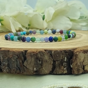 May include: A beaded bracelet featuring a variety of colorful gemstones. The bracelet is composed of small, round beads in shades of blue, green, purple, yellow, and clear. The bracelet is displayed on a wooden surface.