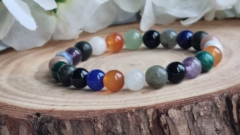 May include: A bracelet made of various colored gemstone beads, including green, blue, purple, orange, white, and black. The bracelet is on a wooden surface.