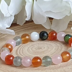 May include: A bracelet made of natural stone beads in various colors, including pink, green, white, and orange. The beads are round and smooth, and the bracelet is strung on a clear elastic cord.