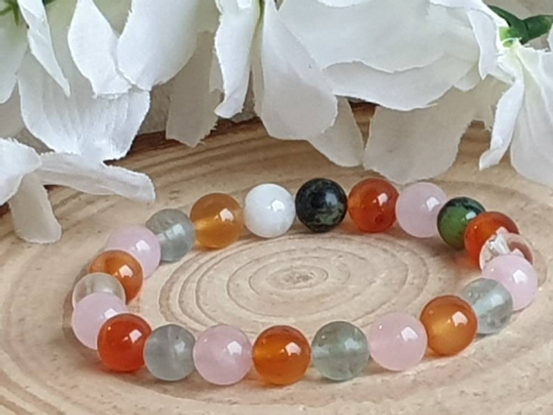 May include: A bracelet made of natural stone beads in various colors, including pink, green, white, and orange. The beads are round and smooth, and the bracelet is strung on a clear elastic cord.