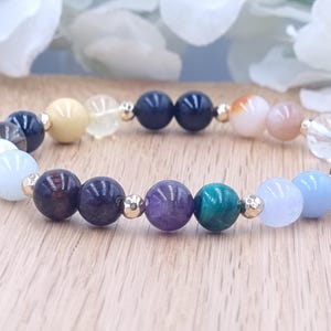May include: A colorful beaded bracelet with various gemstones, including amethyst, aquamarine, and sunstone. The bracelet is made with gold-toned spacers and is strung on elastic.