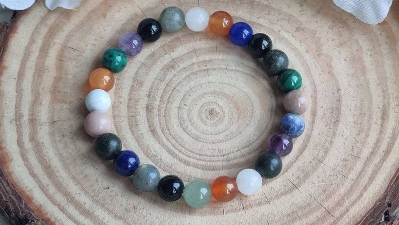 May include: A colorful beaded bracelet with various stones, including black, white, blue, green, and orange. The bracelet is on a wooden surface.