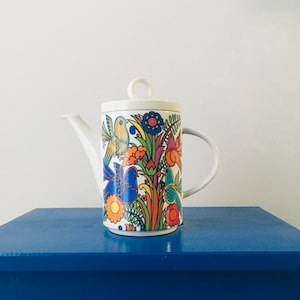 May include: White ceramic teapot with a colourful floral and bird design. The teapot has a lid and a spout. The design features blue, green, yellow, orange, and red colours.
