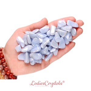 May include: A hand holding a pile of blue lace agate tumbled stones. The stones are smooth and have a light blue color with white banding.