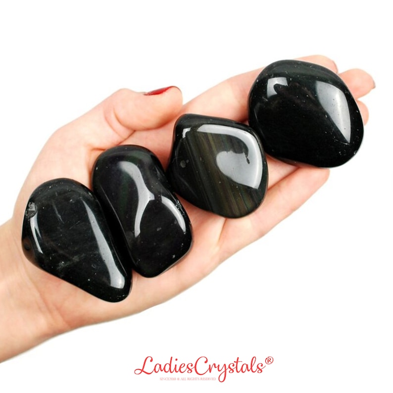 May include: Four smooth, black obsidian tumbled stones with iridescent rainbow flashes. The stones are in a hand, with the fingers spread out.