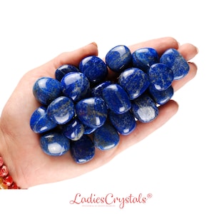 Puede incluir: Una colección de piedras de lapislázuli pulidas de varios tamaños y formas. Las piedras son de color azul intenso con vetas blancas y están dispuestas en una pila en una mano.