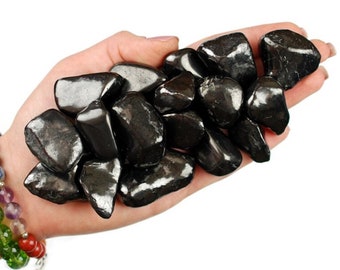 May include: A hand holding a pile of black tumbled stones. The stones are smooth and have a shiny, metallic finish.