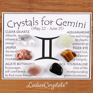 May include: A white card with the text "Crystals for Gemini" and various gemstones. The gemstones include clear quartz, jasper, agate, aquamarine, tiger eye, and black tourmaline. The card also features the Gemini symbol.