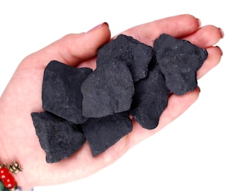 May include: A hand holding a pile of black, rough, and irregularly shaped stones. The stones are likely a type of raw, unpolished crystal.