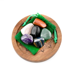 May include: A collection of polished gemstones in various colors, including purple, black, and orange, presented on a wooden tray with a green pouch. The tray has a decorative floral design. The gemstones are of different shapes and sizes.