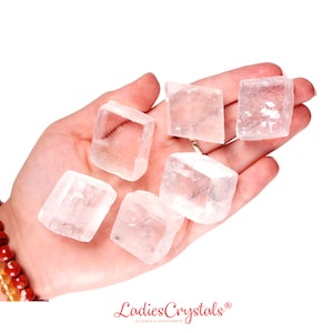 Könnte beinhalten: Eine Hand hält sechs klare, weiße Selenit-Kristallwürfel. Die Kristalle sind glatt und haben ein natürliches, poliertes Aussehen.